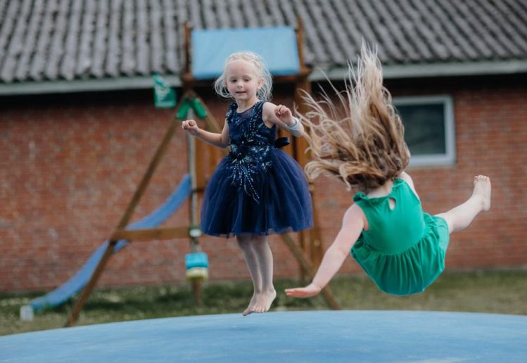 Two girls enjoy jumping on a trampoline outside. Fun and laughter in a playful setting.