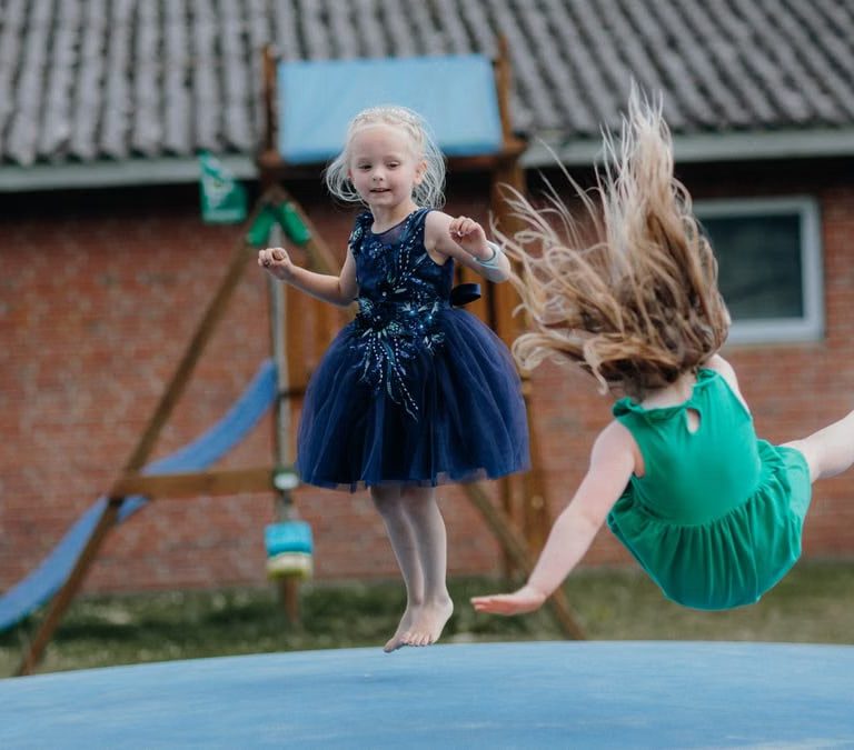 Two girls enjoy jumping on a trampoline outside. Fun and laughter in a playful setting.