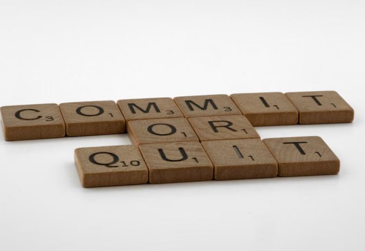 Scrabble tiles spelling 'Commit Or Quit' on a white surface, symbolizing decision-making.