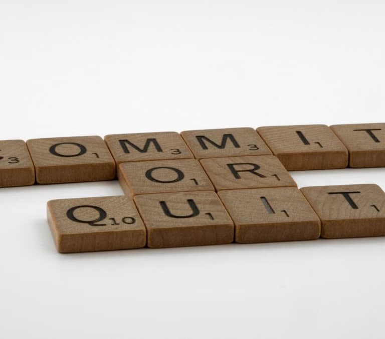 Scrabble tiles spelling 'Commit Or Quit' on a white surface, symbolizing decision-making.